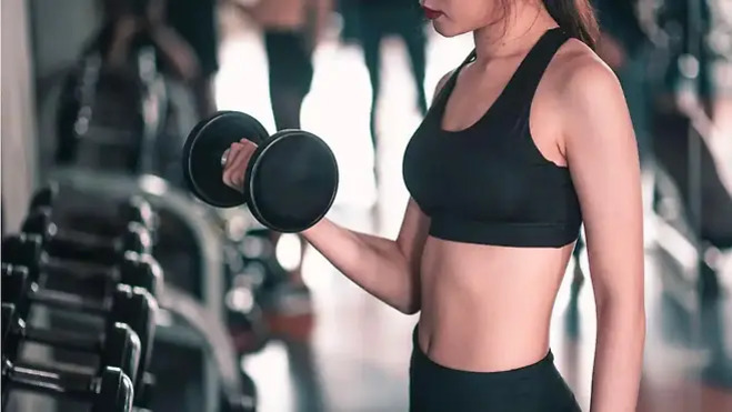 운동복을 입은 여성이 헬스장에서 아령을 들고 운동하고 있다.