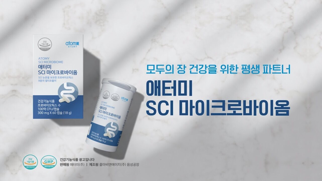 흰색 대리석 배경 위에 애터미 SCI 마이크로바이옴 건강기능식품 박스와 캡슐 용기가 놓여 있고, 오른쪽에는 '모두의 장 건강을 위한 평생 파트너 애터미 SCI 마이크로바이옴'이라는 문구가 파란색 글씨로 적혀 있다.