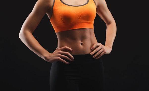 운동복을 입은 여성의 상반신이 검은 배경 앞에 보인다. 오렌지색 스포츠 브라와 검은색 레깅스를 착용하고 있다.